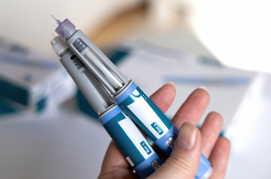 A close-up of a hand holding two GLP-1 injection pens, with visible dosage markings of 1 mg.