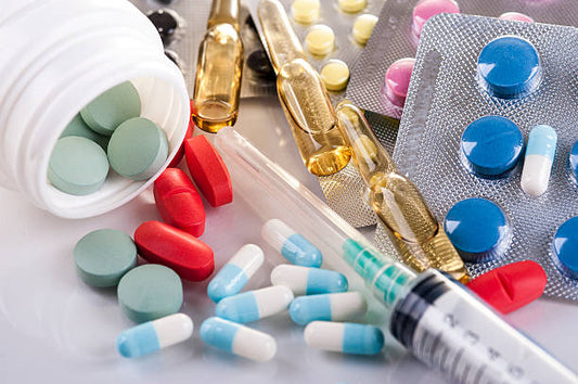 A collection of various medications, including colorful tablets, capsules, blister packs, glass ampoules, and a syringe.